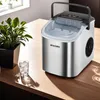 An ice maker sits on a wooden table next to a potted plant and a glass of ice water. Voir les images du produit