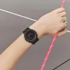 A person's arm wearing a black watch with red accents is shown, with a pink rope in the foreground. Voir les images du produit