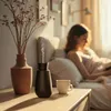 A woman is reading a book in bed, with an aroma diffuser and a vase of dried flowers on a bedside table. Náhľad obrázku produktu