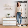 A woman stands next to a dresser with shelves above it, with a height measurement scale on the right. Produktbild-Vorschau