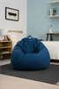 A blue bean bag chair is placed on a dark rug in a bedroom setting, next to a bed and a nightstand. Voir les images du produit