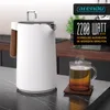A white electric kettle with a wooden-look handle sits on a marble countertop next to a mug of tea, with kitchen cabinets and a faucet in the background. Voir les images du produit