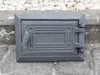 A dark gray cast iron door with a decorative pattern, likely for a chimney or oven, is placed on a stone surface. Náhled obrázku produktu