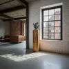 Interior shot of a modern loft-style living space with exposed brick and industrial elements. A wooden pedestal with a decorative sculpture is placed near a large window overlooking a city street. Voir les images du produit