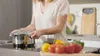 A person is cooking in a kitchen, with vegetables in the foreground. Anteprima dell’immagine prodotto