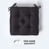 A black tufted seat cushion with ties, shown from a top-down perspective on a light gray background. A graphic illustrating hand-stitching is present in the lower left corner. Anteprima dell’immagine prodotto