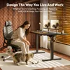 A woman is sitting in an office chair and playing with her cat next to a standing desk. Náhled obrázku produktu