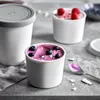 Three white ice cream containers filled with pink ice cream and topped with blueberries and raspberries, placed on a gray surface. Produktbild-Vorschau
