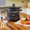 A black Russell Hobbs slow cooker with 'Lasagne' written on it in chalk, placed on a wooden countertop with ingredients like onions, tomatoes, and cheese nearby. Podgląd zdjęcia produktu