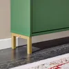 Close-up of the bottom part of a green cabinet with gold legs, placed on a dark wooden floor. Náhľad obrázku produktu