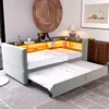 A modern living room or bedroom with a light gray sofa bed extended with a pull-out mattress, featuring built-in LED lighting and shelves with decorative items and a tablet. Produktbild-Vorschau