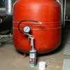 A can of foam filler with a pressure gauge and spray gun attached to a large red expansion tank. Produktbild-Vorschau