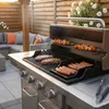 A barbecue grill with steaks, sausages, and skewers cooking on it, set in an outdoor patio area with seating. Podgląd zdjęcia produktu