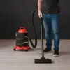 A person is using a KAMINER ash vacuum cleaner on a wooden floor in front of a dark gray wall. Produktbild-Vorschau