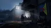 A group of people in a dimly lit outdoor setting, possibly a village square at night, with a flag hanging on a building. Produktbild-Vorschau