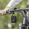 A person's hand is holding the handlebars of a bicycle, with a small black Bluetooth speaker hanging from the handlebars. Voir les images du produit