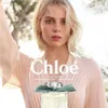 A woman is shown in a soft, natural setting, with a bottle of Chloé Rose Naturelle Intense Eau De Parfum prominently displayed. Náhled obrázku produktu