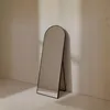 A full-length mirror with a black frame stands against a light-colored wall, with soft shadows cast on the wall. Produktbild-Vorschau