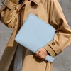 A person wearing a tan trench coat holds a light blue laptop sleeve. Produktbild-Vorschau