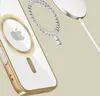 A close-up, angled view of a gold and clear iPhone case with the Apple logo visible, alongside a disassembled magnetic charging ring and a white wireless charger with a white cable. Podgląd zdjęcia produktu