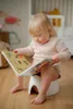A young child sits on a potty and reads a book. Produktbild-Vorschau