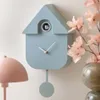 A modern cuckoo clock is displayed on a wall next to a pink lamp and a vase of pink flowers. Náhled obrázku produktu