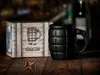 A black grenade-shaped mug and its packaging sit on a wooden surface. Voir les images du produit