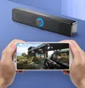 A person is holding a smartphone displaying a video game, with a computer soundbar in the background. Voir les images du produit
