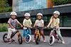 Four children wearing helmets are posing with their balance bikes outdoors. Produktbild-Vorschau