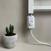A close-up of a white electric heating element attached to a white radiator, with a small potted cactus in a gray pot to the left. Anteprima dell’immagine prodotto