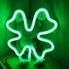 A neon sign shaped like a four-leaf clover is displayed in front of a stuffed frog. Produktbild-Vorschau