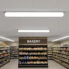 Interior view of a supermarket bakery section with shelves stocked with bread and other baked goods, and aisles of groceries visible in the background. Overhead fluorescent lights illuminate the scene. Produktbild-Vorschau