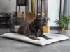 A dark-colored dog lies on a soft, gray and white pet mat in a home environment. Voir les images du produit
