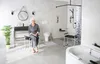 A woman sits on a stool in a modern, accessible bathroom. Produktbild-Vorschau