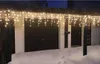 Icicle lights are hung on the eaves of a house over a snowy driveway with two garage doors. Produktbild-Vorschau