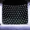 A net of white LED lights is strung between two white pillars, illuminating a dark background with some greenery visible behind the lights. The ground in front is paved. Produktbild-Vorschau