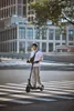 A man rides an electric scooter across a crosswalk in a city. Produktbild-Vorschau