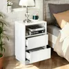 A white nightstand with two drawers and an open shelf, placed next to a bed. Náhled obrázku produktu