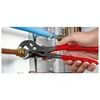 A hand is using Knipex Cobra pliers to grip a copper pipe fitting. Other plumbing pipes are visible in the background. Anteprima dell’immagine prodotto