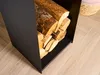 A close-up shot of a black metal log holder filled with firewood, placed on a light-colored wooden floor. A woven basket is partially visible in the background. Anteprima dell’immagine prodotto
