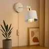 A wall lamp is mounted on a wall next to a potted plant and a framed picture. Náhled obrázku produktu