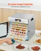 A person is pulling out a tray from a food dehydrator filled with various dried fruits and meats. Finished dried food is on plates in the foreground. Podgląd zdjęcia produktu