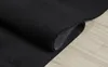 A black rug is partially rolled up on a light-colored wooden floor. Produktbild-Vorschau