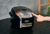 A finger presses a button on a black rice cooker with a digital display. Produktbild-Vorschau