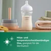 A glass baby bottle filled with milk sits on a wooden surface next to a wooden stacking toy and folded towels. Podgląd zdjęcia produktu