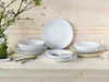 A set of white porcelain plates and bowls are arranged on a wooden surface, with a vase of flowers in the background. Produktbild-Vorschau