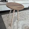 A small, oval wooden side table with three light-colored wooden legs sits on a fluffy beige rug next to a white sofa. Produktbild-Vorschau