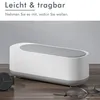 A white and gray ultrasonic cleaner is displayed on a wooden surface, with a watch and glasses nearby. Produktbild-Vorschau