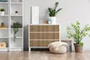 A dresser with a wooden slatted front is placed next to a white bookshelf and a potted plant in a room. Podgląd zdjęcia produktu