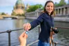 A woman is handing a memory card to someone off-camera, with a city skyline and river in the background. Produktbild-Vorschau